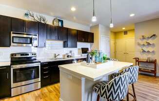 Eat in kitchen with black cabinetry, sleek stainless steel appliances, and pendant lights.