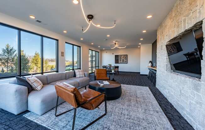 Carmel, IN, Apartments Near Monon Trail - North End - Clubroom with Carpeted Flooring, Couch, Armchairs, Coffee Table, TV, Kitchen Area, and Floor-to-Ceiling Windows.