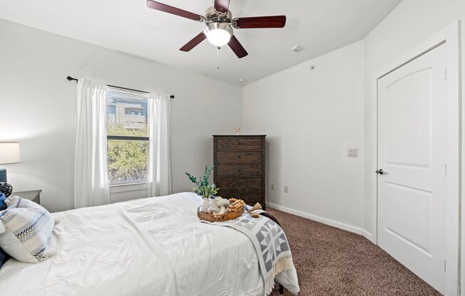 A bedroom with a bed, a ceiling fan, and a window with curtains.