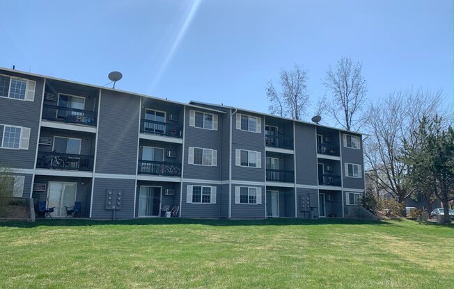 a grey apartment building with a green lawn in front of it