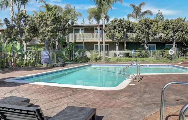 A pool surrounded by palm trees and a building in the background.