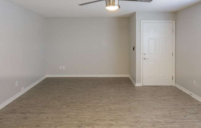 an empty living room with a ceiling fan and a white door