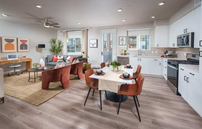 Garden-Style Apartments in Rancho Cordova, CA with an In-Unit Washer and Dryer - Aurora - Open Living Room with Vinyl Plank Flooring, Area Rug, Couch, Armchairs, Coffee Table, Ceiling Fan, Dining Area with Four-Seater Table, Kitchen with White Cabinets, and Stainless Steel Appliances.