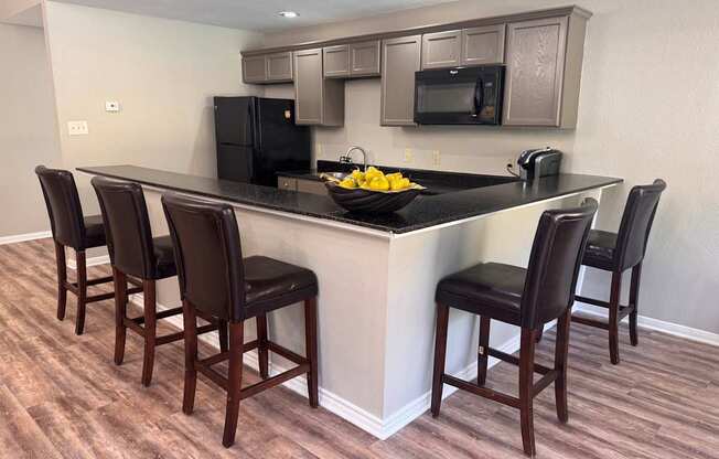 A kitchen with a black counter top and brown chairs.