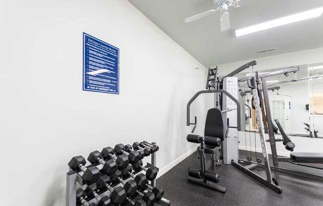 A gym with a variety of equipment including dumbbells, a bench, and a weight machine.