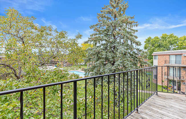 A balcony with a black railing overlooks a pool and trees.