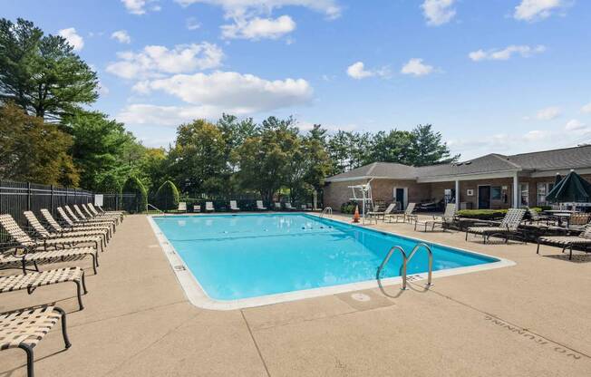 A large outdoor swimming pool surrounded by lounge chairs and trees.
