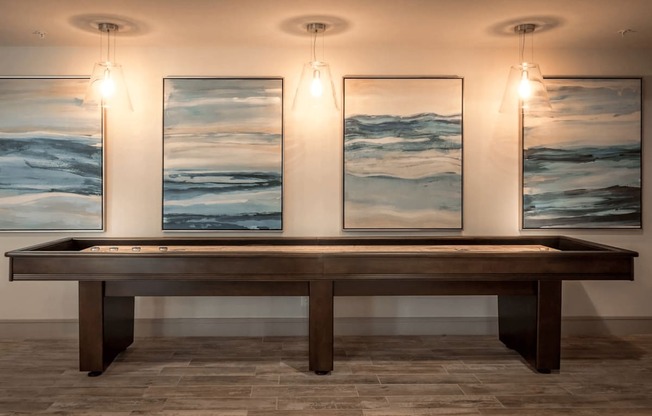 A long brown table is in front of three framed landscape paintings.