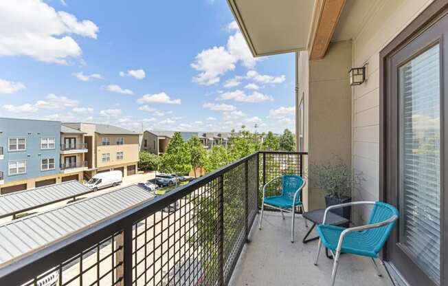 a balcony with two blue chairs and a table and a building in the background