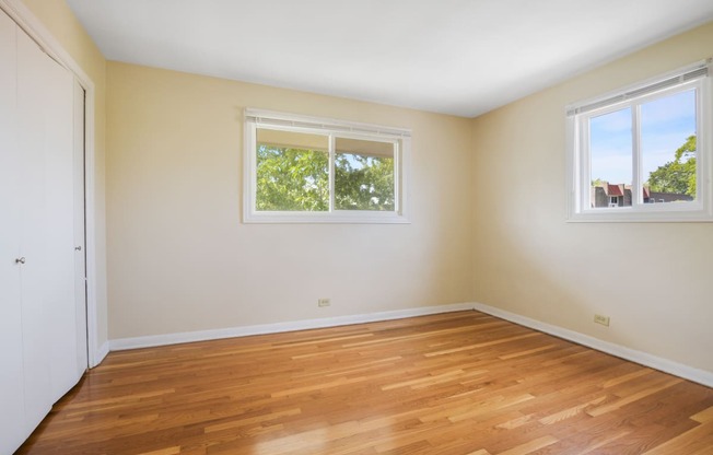 an empty room with wooden floors and two windows