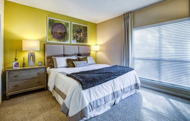 Model bedroom at our apartments in Nashville, featuring carpeted flooring and a large window with blinds.