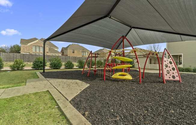 a playground with swings and a swing set under a shade