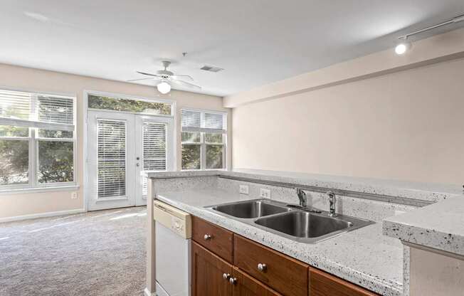 The kitchen of Ten05 West Trade Apartments, featuring a cut-down counter with a stainless steel sink and a dishwasher, plus plenty of natural sunlight through high windows and the patio door.