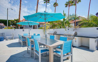 a patio with a grill and tables with blue chairs and umbrellas at Laguna Gardens Apts., Laguna Niguel