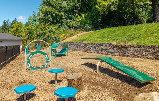 A playground with a green bench, blue and green play equipment, and a brown fence.