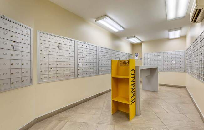 A yellow City Paper newspaper stand in a hallway with rows of mailboxes.