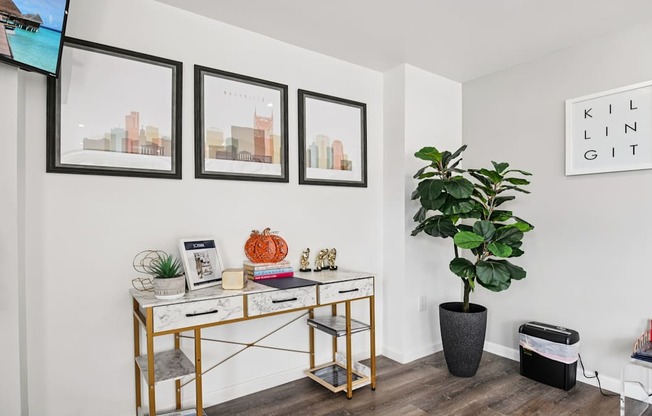 A room with a desk, chair, potted plant, and pictures on the wall.