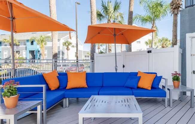 a patio with a blue couch and orange pillows and umbrellas