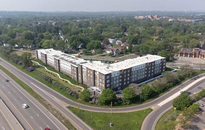 A large building with a white roof is surrounded by trees and a highway.