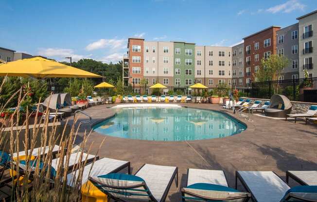 a swimming pool with chairs and umbrellas in front of an apartment building