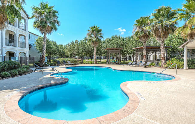 A large swimming pool surrounded by palm trees and a white building.