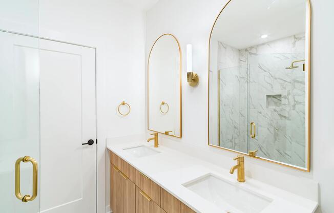 A bright primary bath at Modera Nations in Nashville pairs sleek double vanities, warm brass accents, and refined finishes for a polished daily routine.