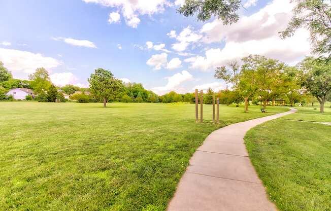 a sidewalk running through a park with grass and trees