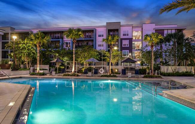 a swimming pool at night with a hotel in the background