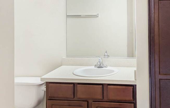 A white sink is on a brown cabinet under a mirror with lights.