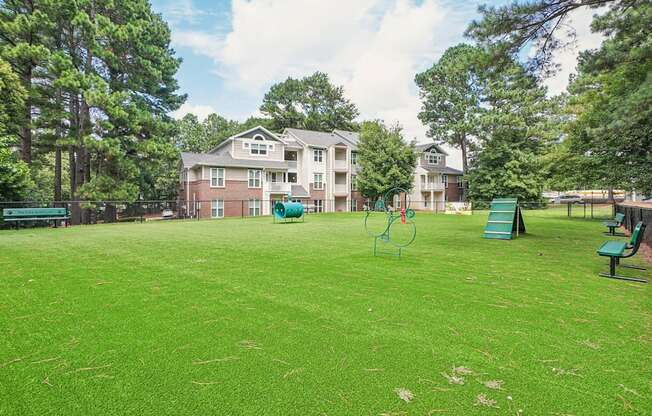 A grassy field with a playground and apartment buildings in the background at The Falls Apartments in Raleigh NC