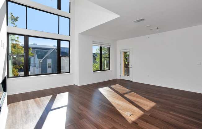 a living room with white walls and wood floors and large windows