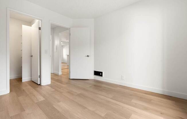 A room with white walls and wooden flooring with two open doors.
