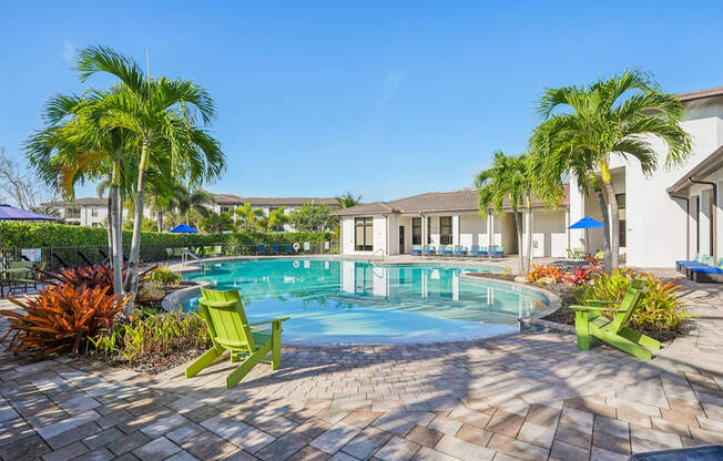 A pool surrounded by palm trees and green chairs.