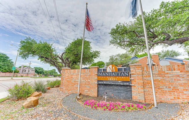 The entrance to a property named Manhattan with a brick wall and a sign.