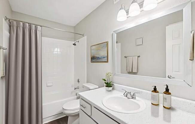 A bathroom with a white sink, toilet, and a grey shower curtain.
