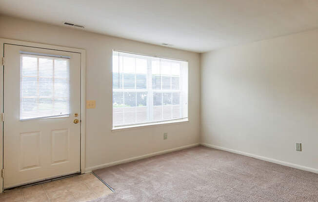 A room with a carpeted floor, a door, and a window with blinds.