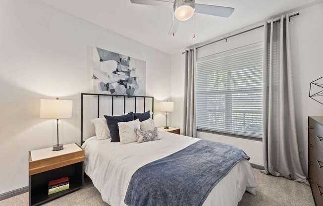 A bedroom with a bed, two lamps, and a painting on the wall.