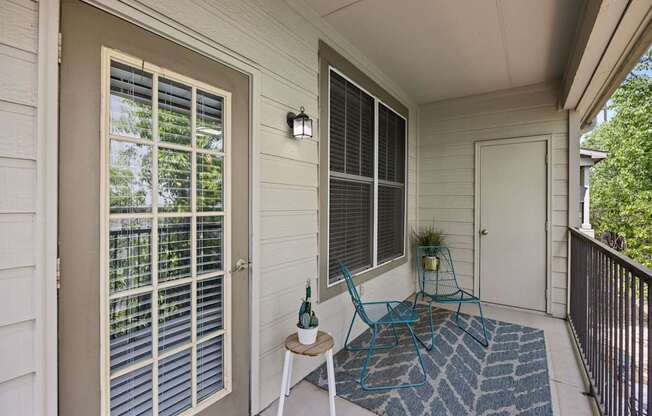 A small balcony with a blue chair and a table with a bottle on it.