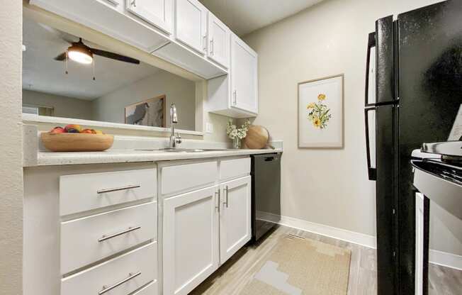 A kitchen with white cabinets and a black fridge.