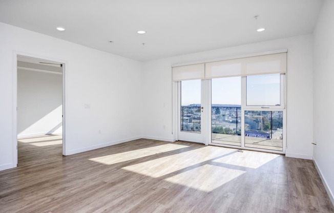 a living room with white walls and wooden floors and a door to a balcony