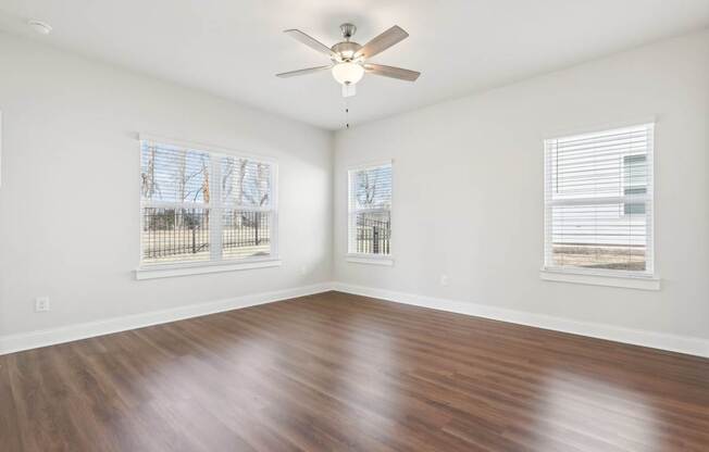 A room with a ceiling fan and two windows.