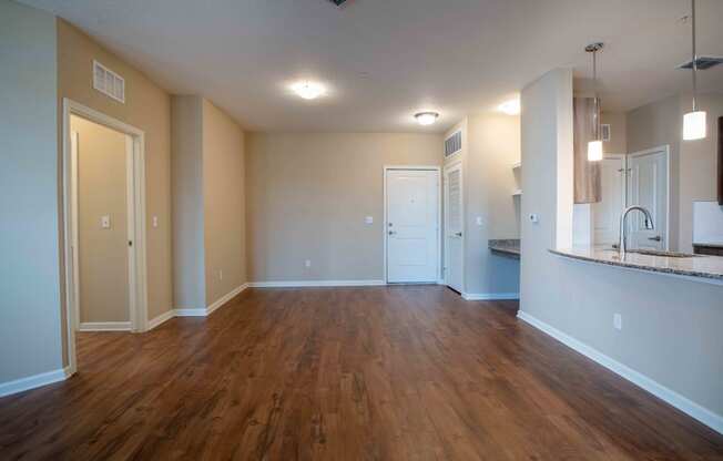 an empty living room with wood flooring and a kitchen