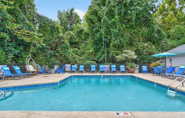 A pool surrounded by trees and chairs.at Lofts of Wilmington Apartments, Wilmington, North Carolina