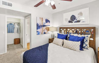 A bedroom with a bed, pillows, a ceiling fan, and a painting on the wall.