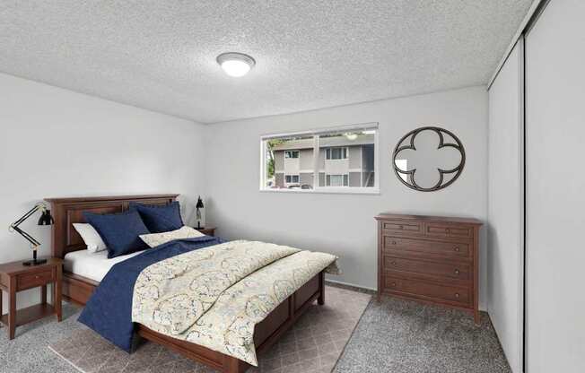 A bedroom with a bed, nightstand, and a window with a view of a building outside.
