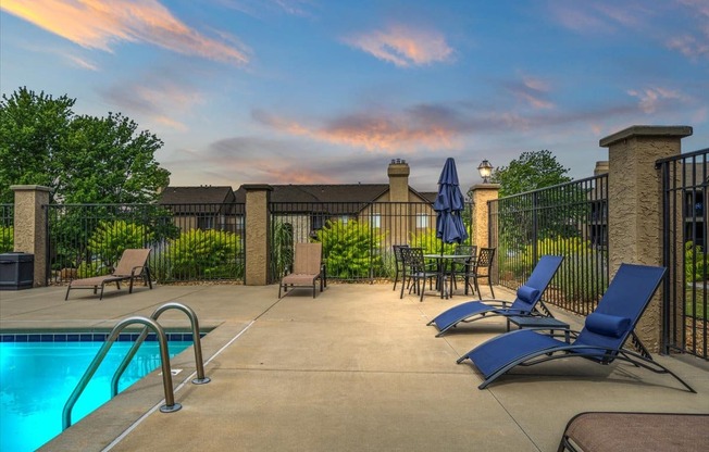 a swimming pool with blue chairs and umbrellas and a fence
