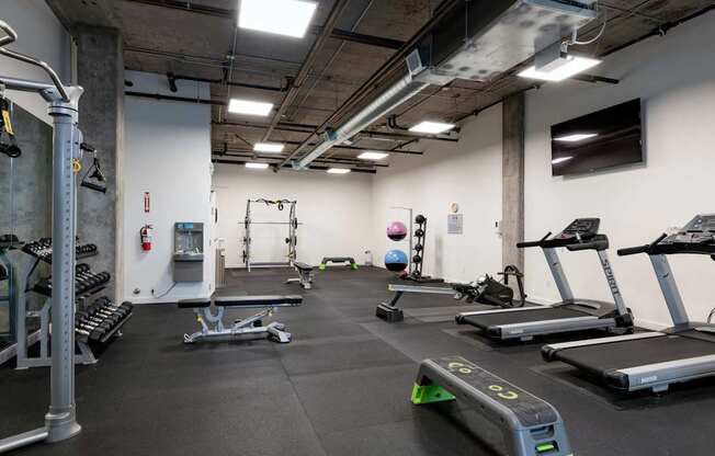A gym with a variety of equipment including treadmills, weights, and exercise machines.