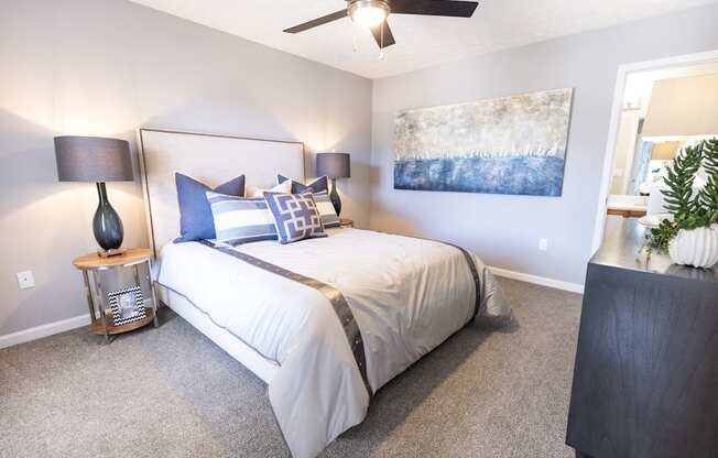 A bedroom with a bed, two lamps, and a painting on the wall.