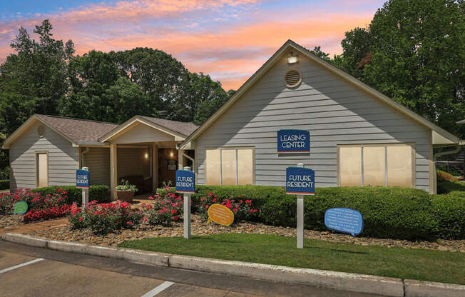 A leasing office with lush landscaping and flowers with future resident parking in front of it at Gwinnett Square Apartments in Duluth, GA