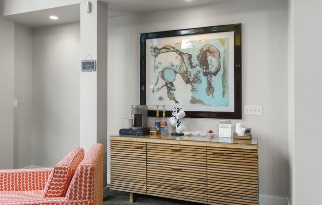 A painting hangs on the wall above a wooden cabinet with a red couch in front of it.